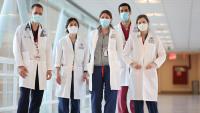 Five doctors stand in a hallway wearing medical masks